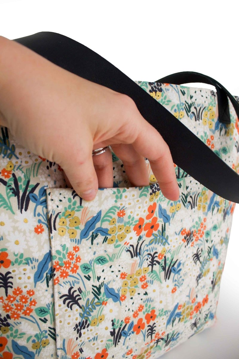Close-up of the tote’s exterior pocket with hand reaching inside, highlighting floral fabric and pocket depth.